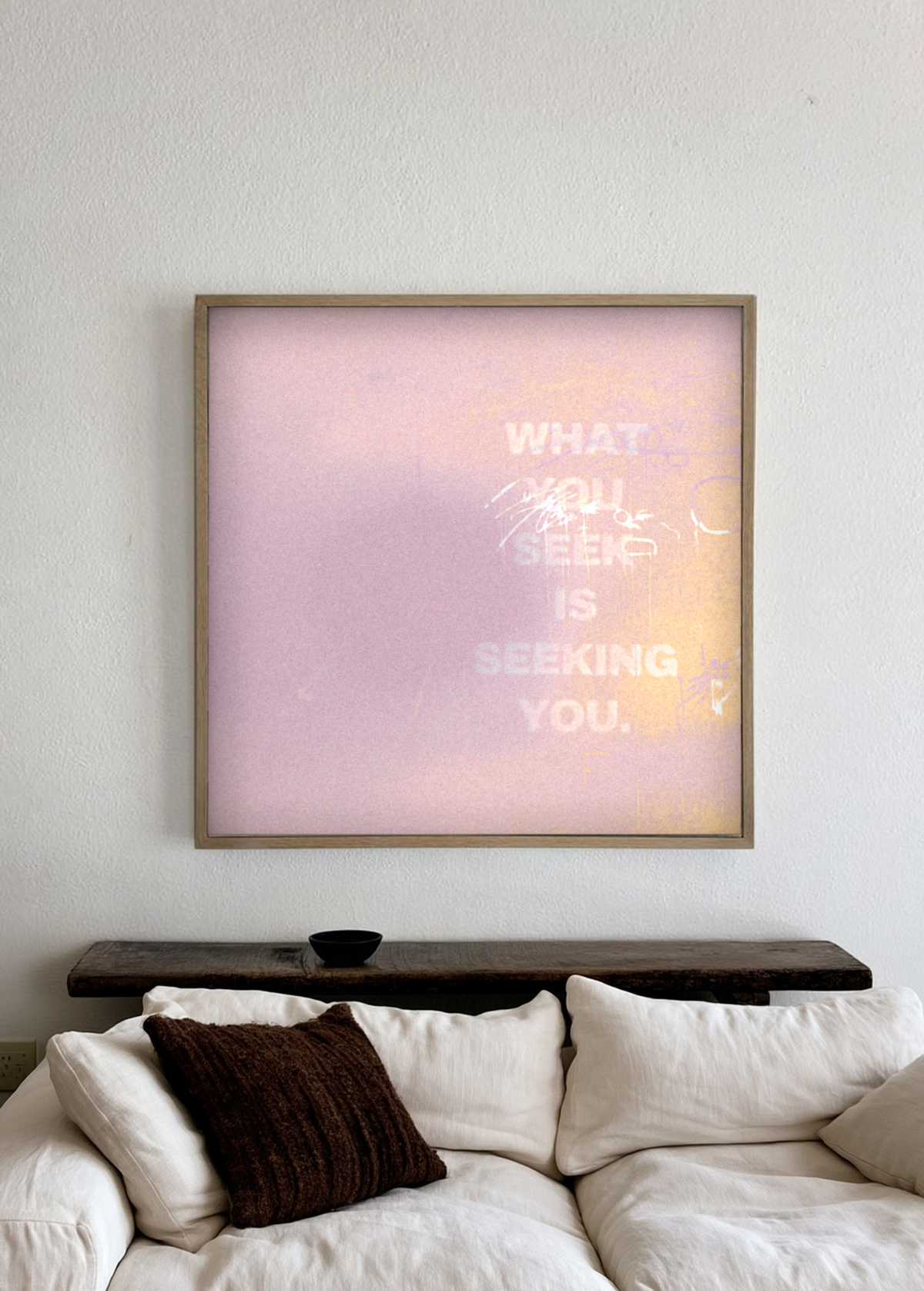 What You Seek pink framed artwork above a white linen sofa and dark wood shelf