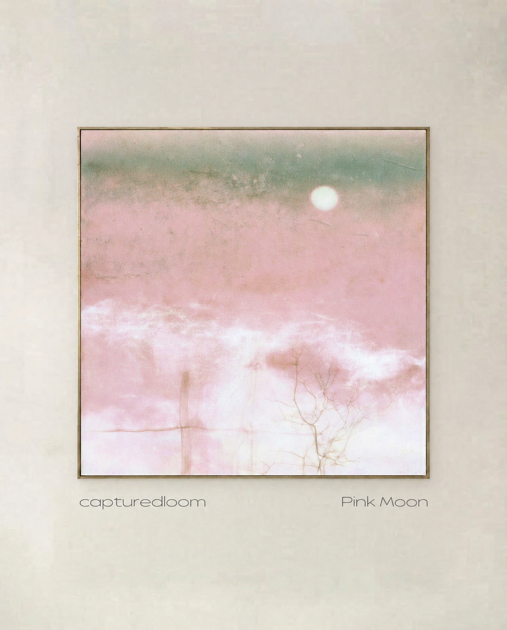 Pink Moon - white moon rising over a blush field with a sea-green horizon, shown in a thin gold frame on a pale wall